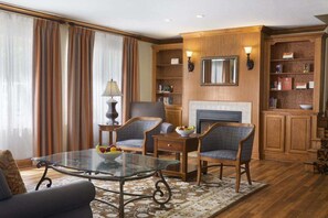 A living room with a glass-top coffee table, two upholstered chairs, a fireplace, and a bookshelf.