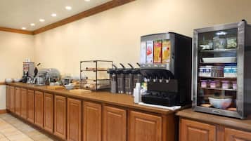 Un buffet de petit-déjeuner en libre-service avec des machines à café, un présentoir réfrigéré et une variété d’aliments.