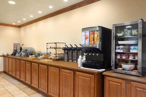 Un mostrador de desayuno tipo buffet con máquinas de café, un refrigerador y una variedad de alimentos.