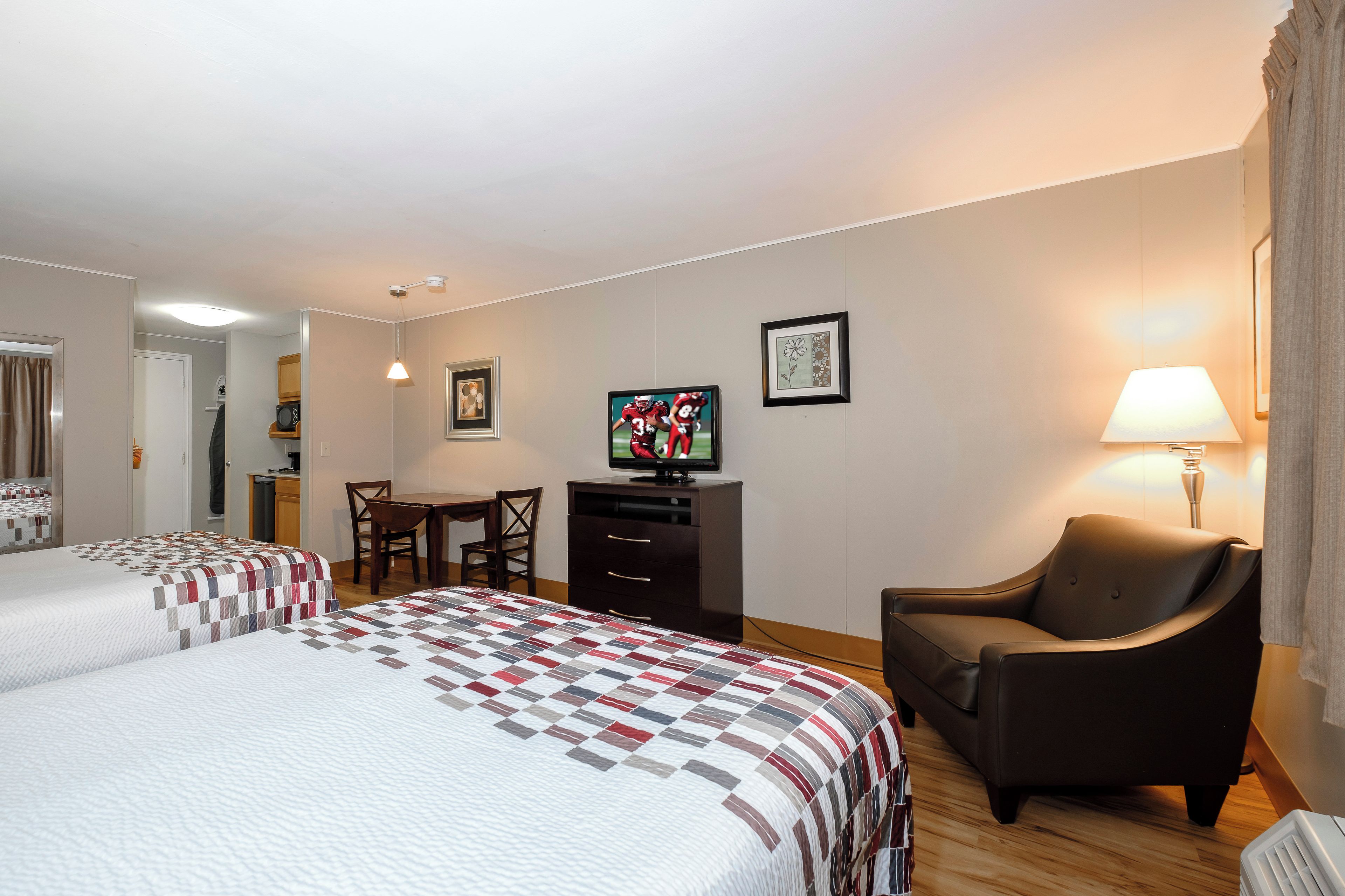 A hotel room with two beds, a desk, a television, and a chair.