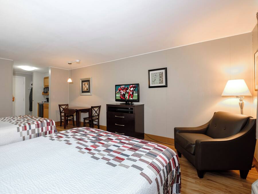A hotel room with two beds, a desk, a television, and a chair.