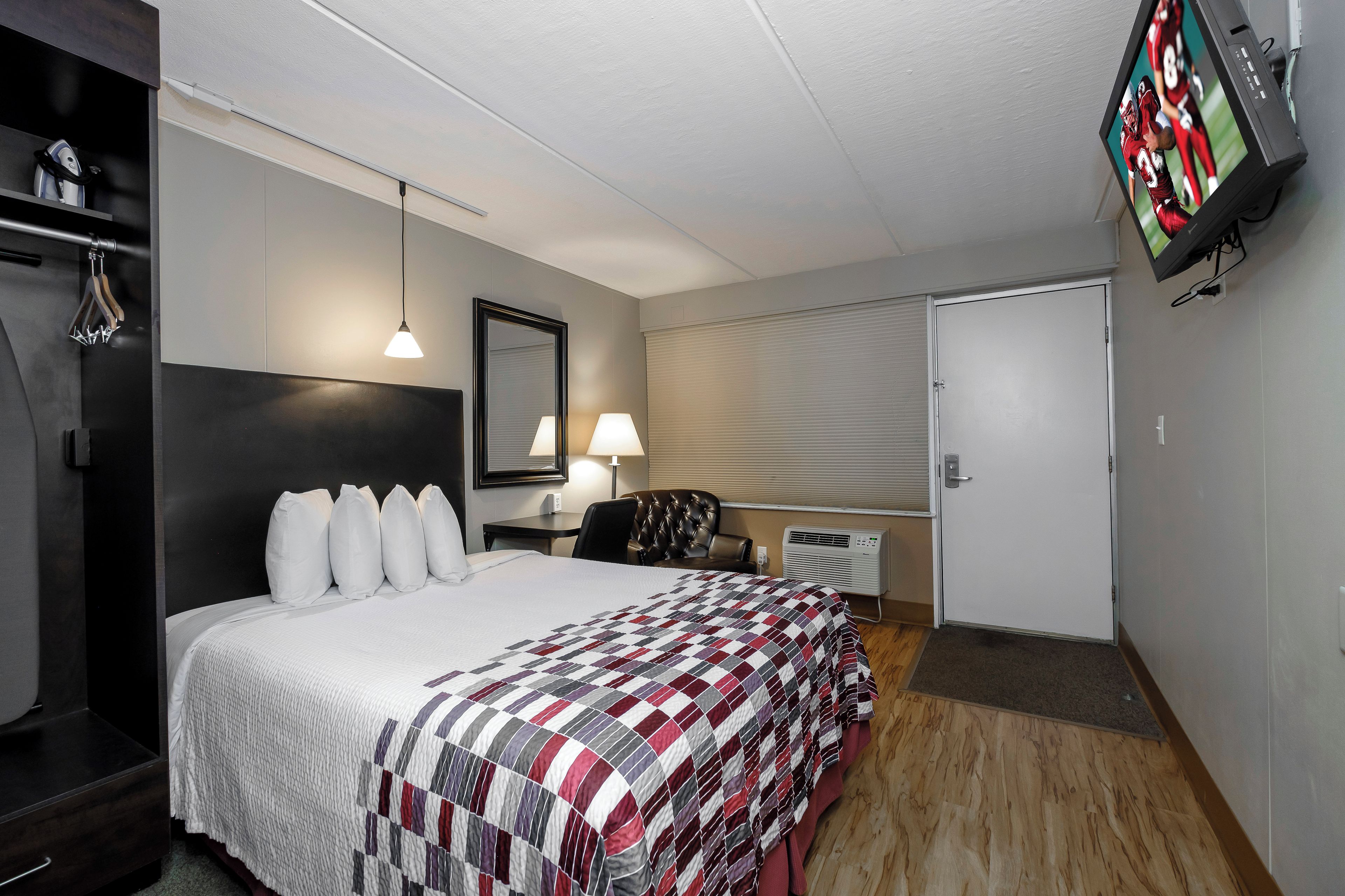 Una habitación de hotel con una cama, un escritorio, una silla, un televisor y un armario.