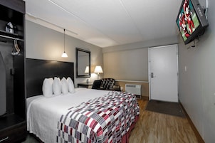 Una habitación de hotel con una cama, un escritorio, una silla, un televisor y un armario.