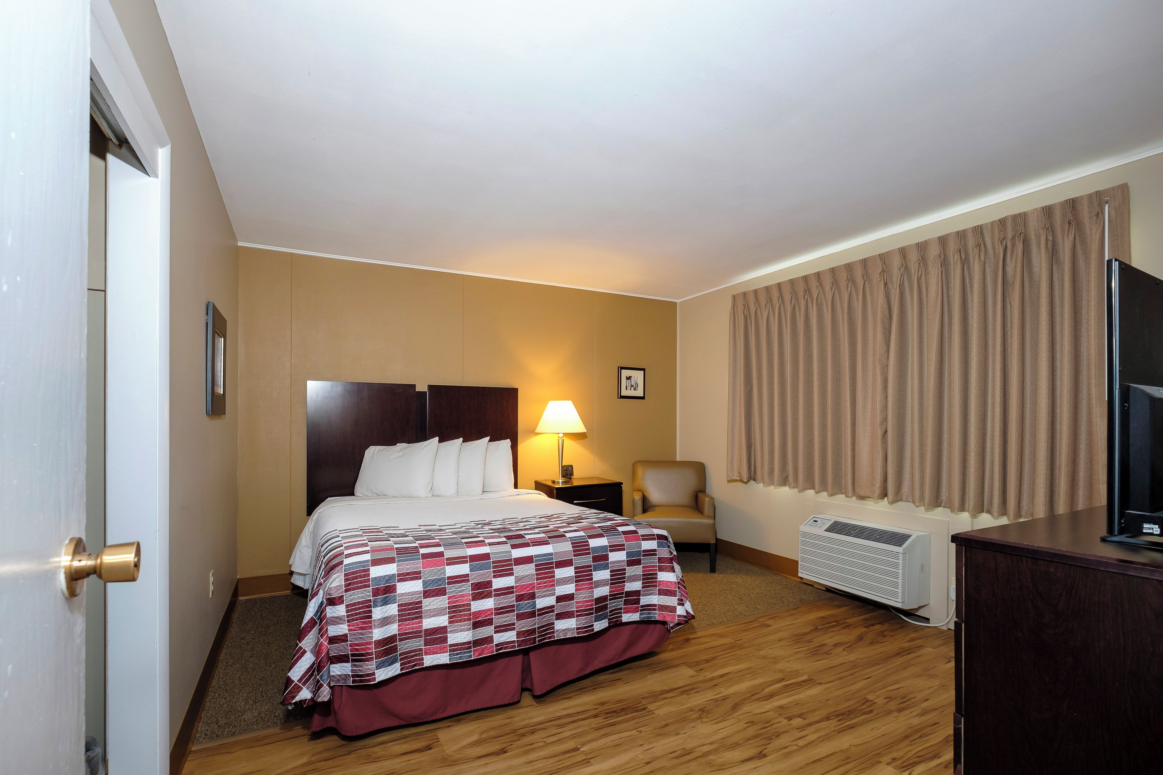 A hotel room with a bed, a chair, a desk, a lamp, and a television.