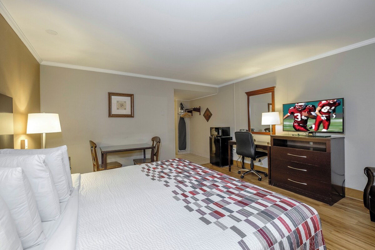 Quarto de hotel com cama, escrivaninha, cadeira, televisão e cômoda.