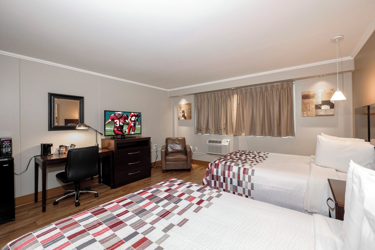 A hotel room with two beds, a desk with a computer, a chair, a TV, and a window with curtains.
