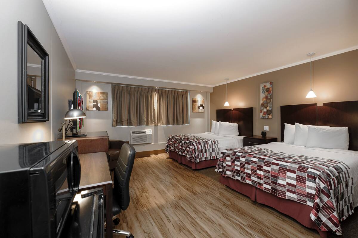 A hotel room with two beds, a desk, a chair, a TV, and a window with curtains.