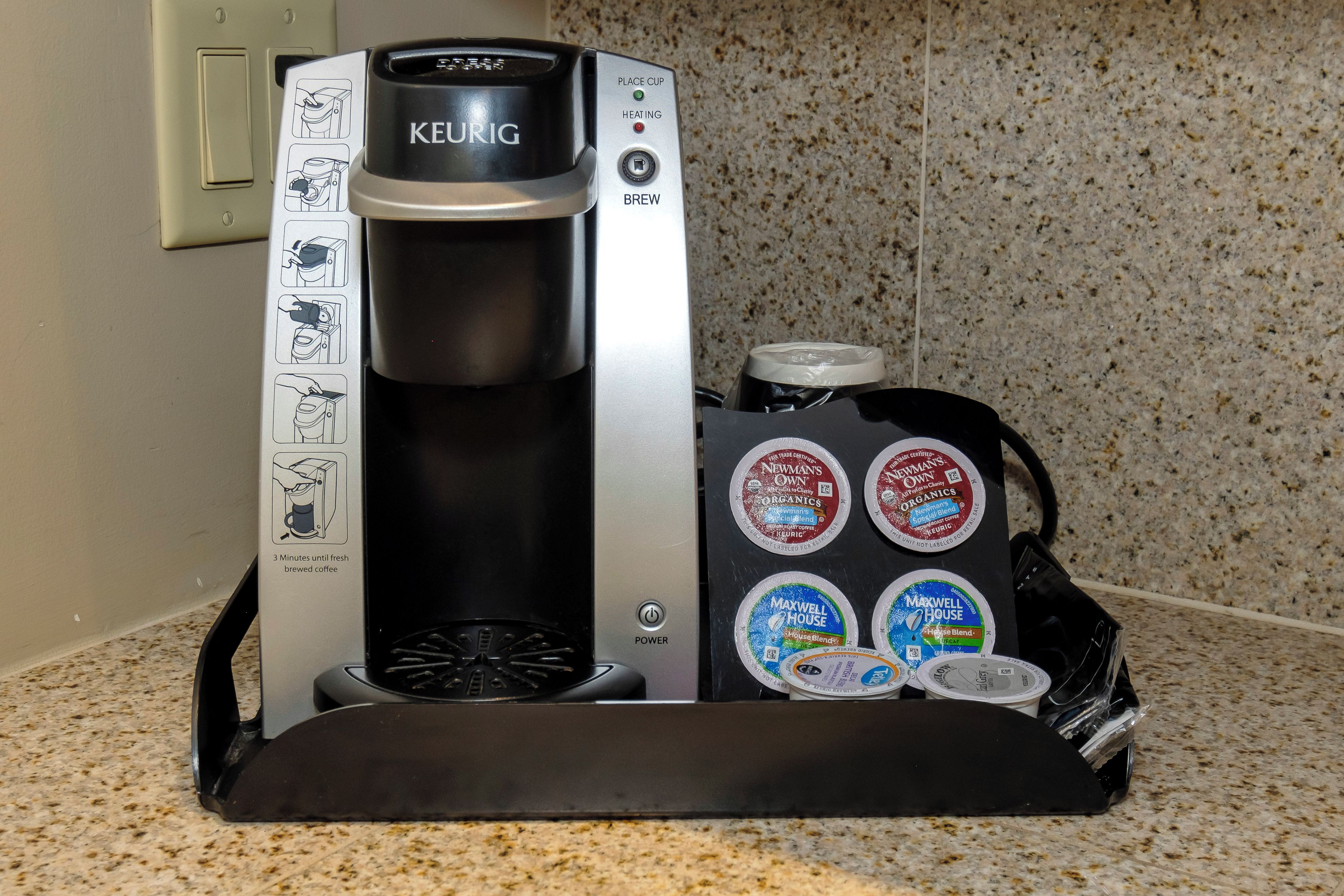 Una cafetera Keurig con un recipiente de goteo y cápsulas de café reutilizables sobre una encimera de cocina.