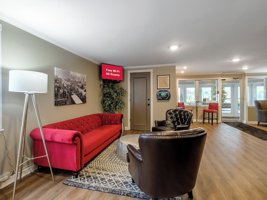 Een moderne woonkamer met een rode bank, een zwarte leren fauteuil, een flatscreentelevisie en een groot raam.