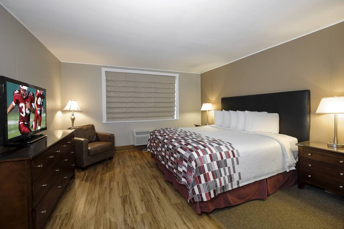 A hotel room with a bed, a television, a desk, and a window with blinds.