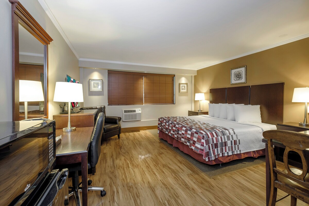 A hotel room with a bed, desk, chair, and a large mirror.
