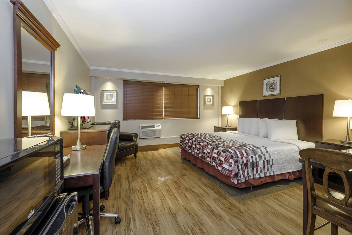 A hotel room with a bed, desk, chair, and a large mirror.