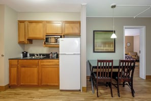 A kitchen with wooden cabinets, a white refrigerator, and a microwave. There is a dining table with chairs and a pendant light. - Red Roof Inn & Suites Herkimer (Herkimer)