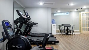 Un gimnasio con cintas de correr, un dispensador de agua y una mesa con sillas.