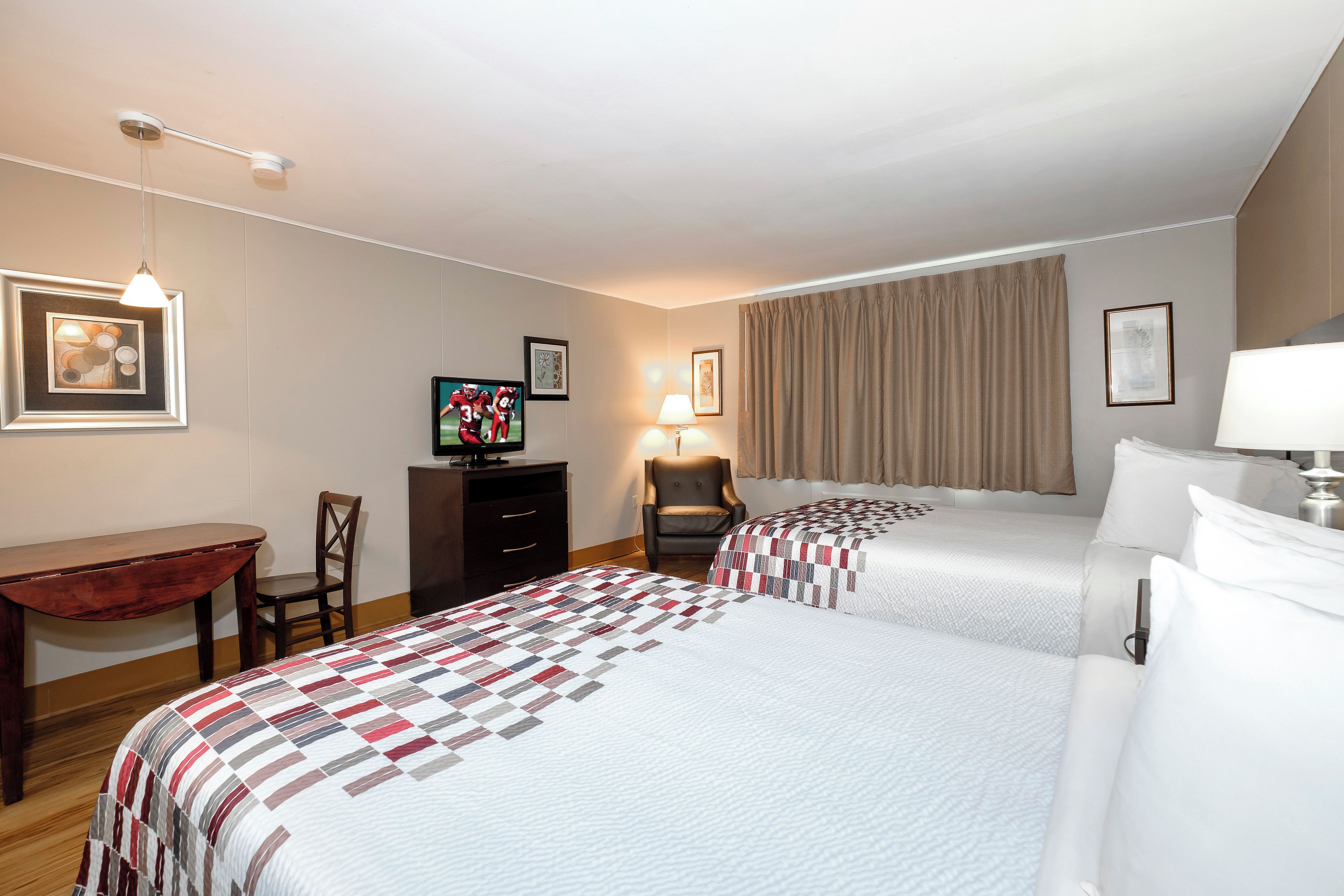 A hotel room with two beds, a desk, a chair, a television, and a lamp.