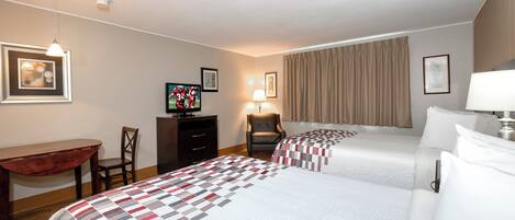 A hotel room with two beds, a desk, a chair, a television, and a lamp.