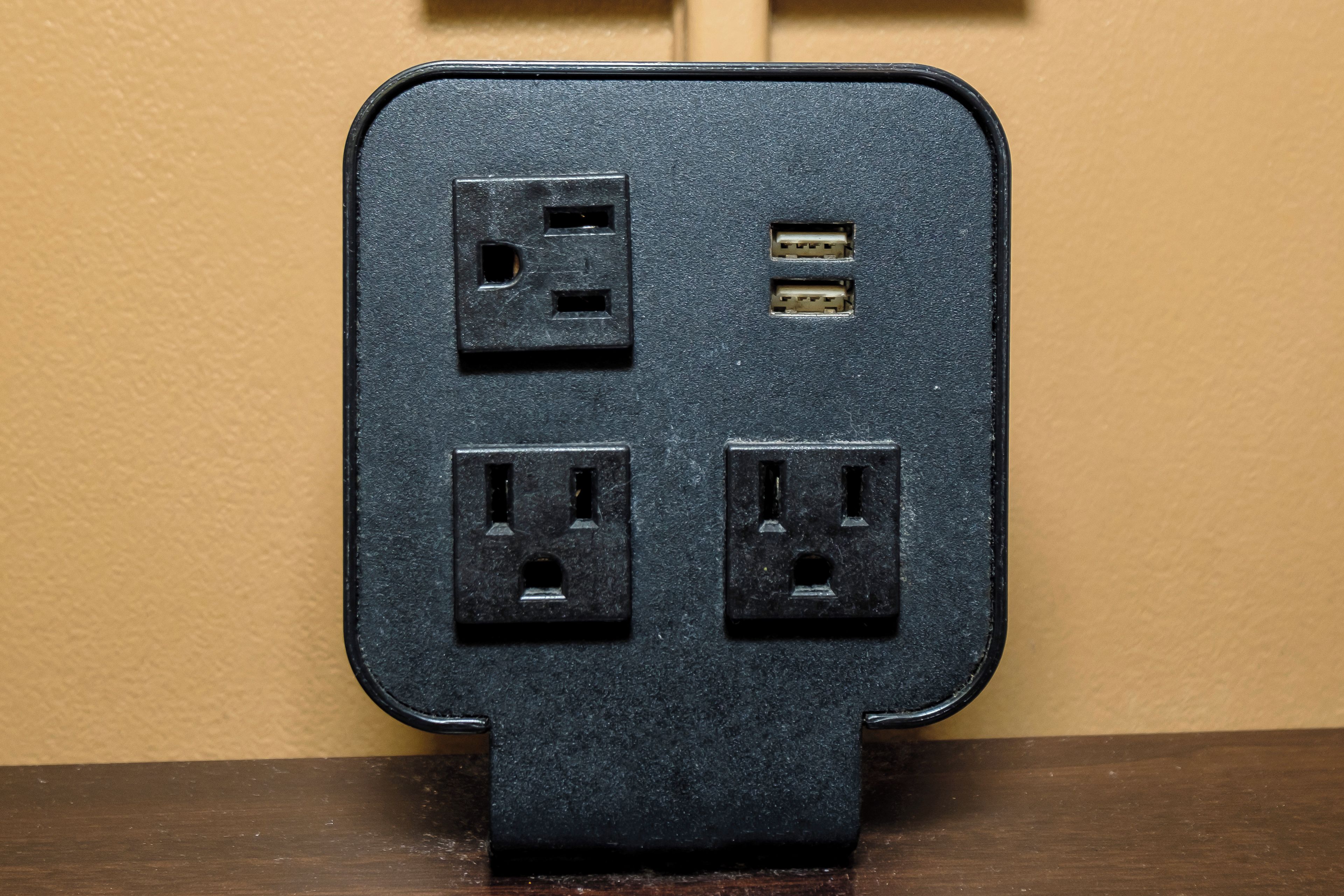 Een zwarte stekkerdoos met vier stopcontacten en een USB-poort, bevestigd aan een muur.