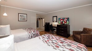 Una habitación de hotel con dos camas, un escritorio con computadora, un televisor y una silla.
