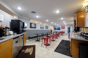 A modern hotel kitchen with stainless steel appliances, a coffee station, and a seating area with red stools.