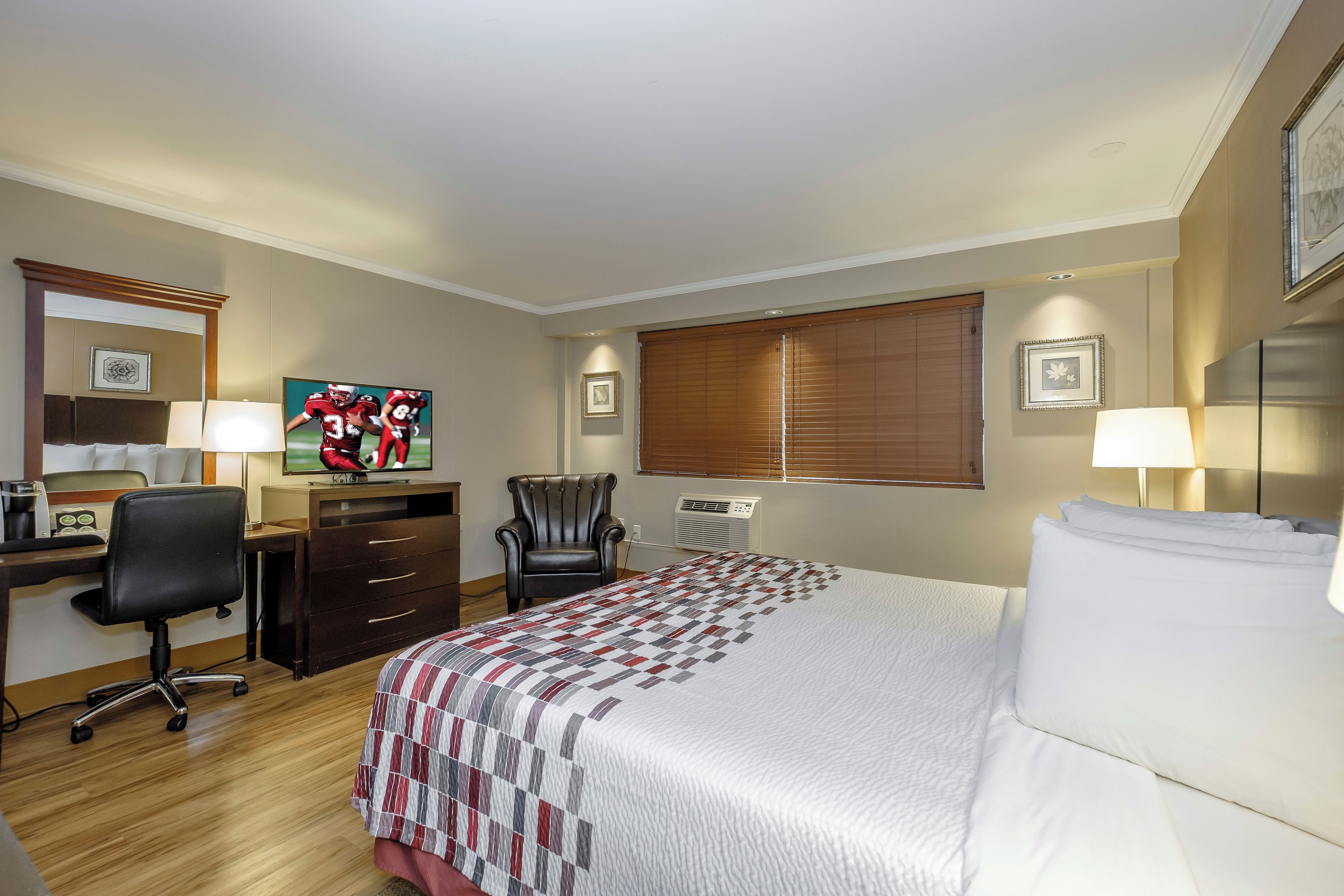 A hotel room with a bed, desk, chair, and a television displaying a sports event.
