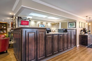A reception area with a dark wood reception desk, a red sign indicating free Wi-Fi, and a marble wall. - Red Roof Inn & Suites Herkimer (Herkimer)