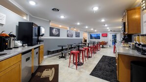 Habitación de hotel moderna con kitchenette, zona de comedor con taburetes rojos y vistas a la ciudad.