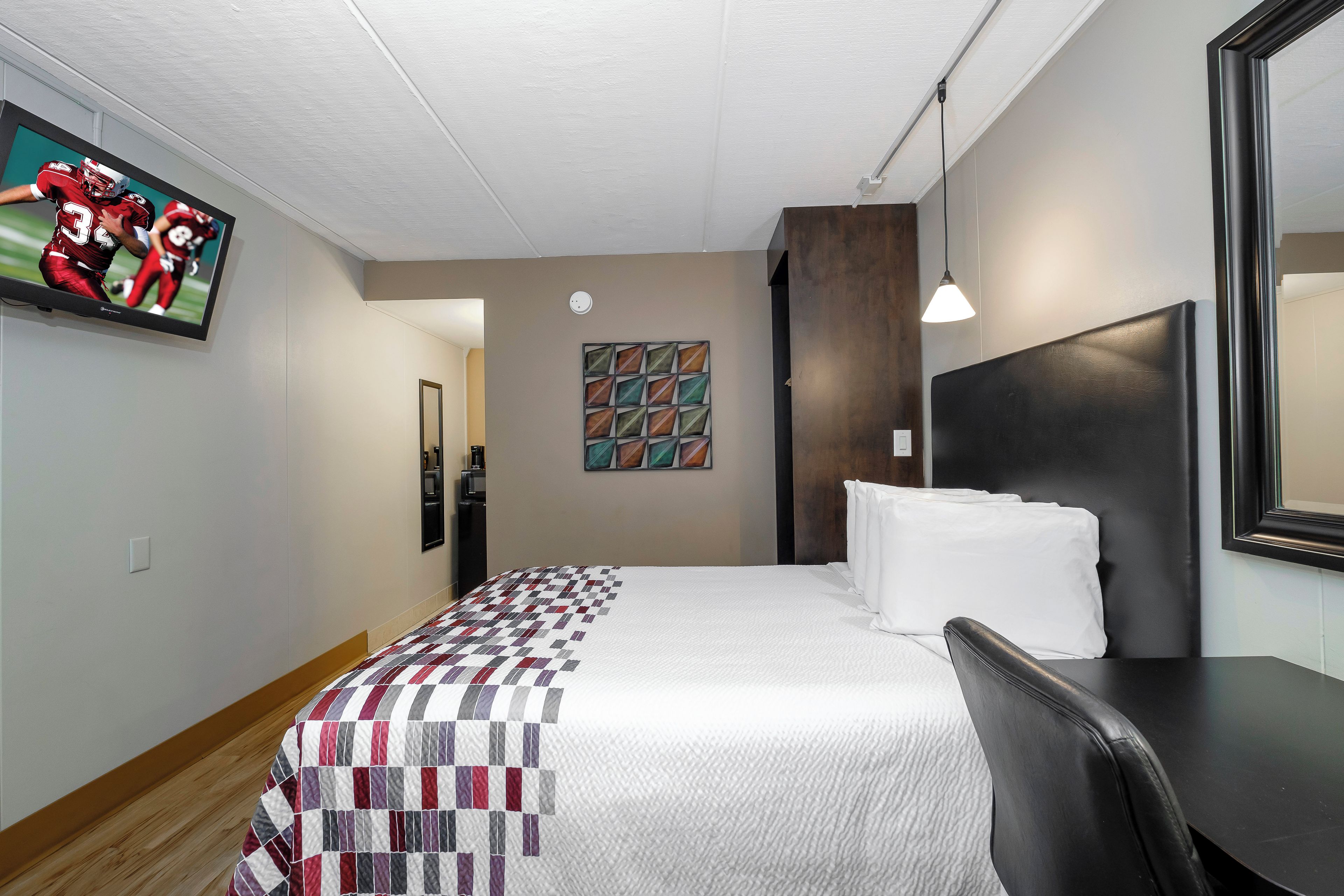 Une chambre d’hôtel avec un lit, un téléviseur fixé au mur, un tableau et un miroir.