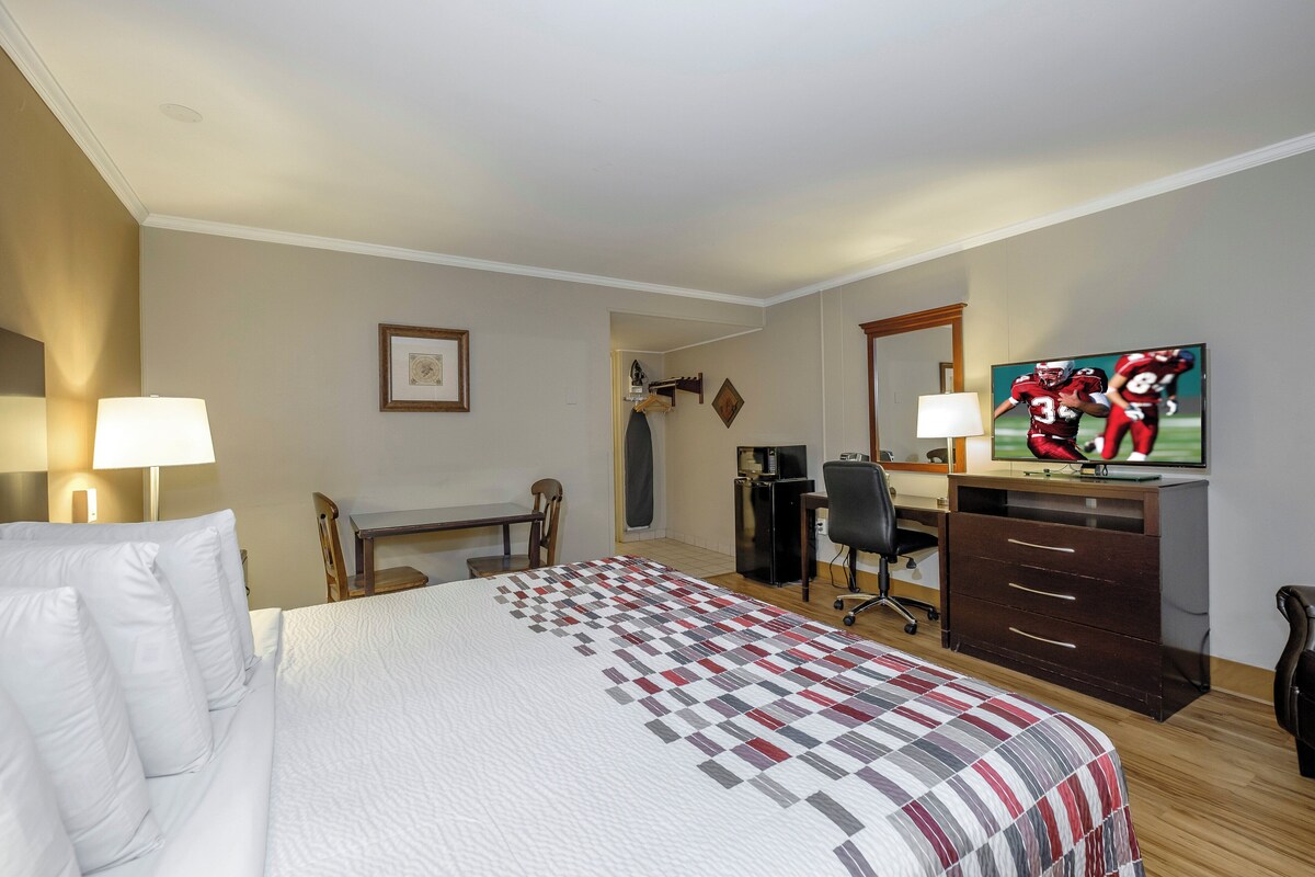 A hotel room with a bed, desk, chair, TV, and dresser.