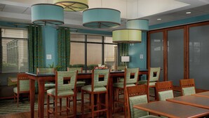 A conference room with wooden tables and chairs, teal curtains, and a large window with blinds.