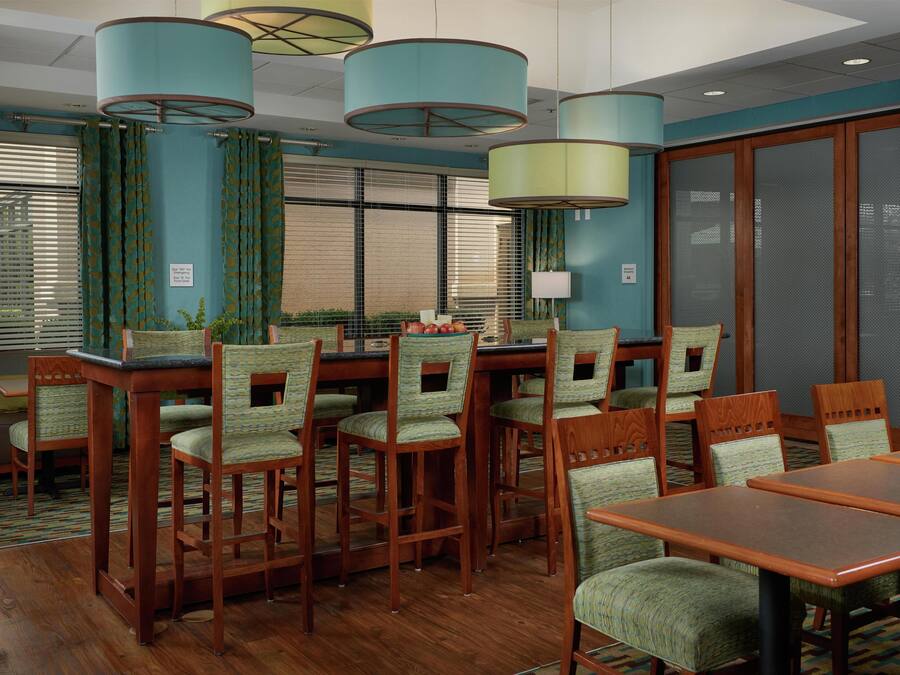 A conference room with wooden tables and chairs, teal curtains, and a large window with blinds.