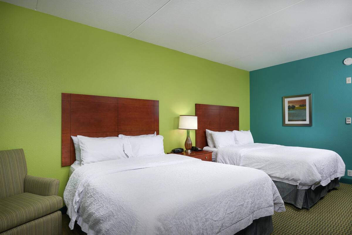 A hotel room with two beds, a green wall, and a wooden headboard.