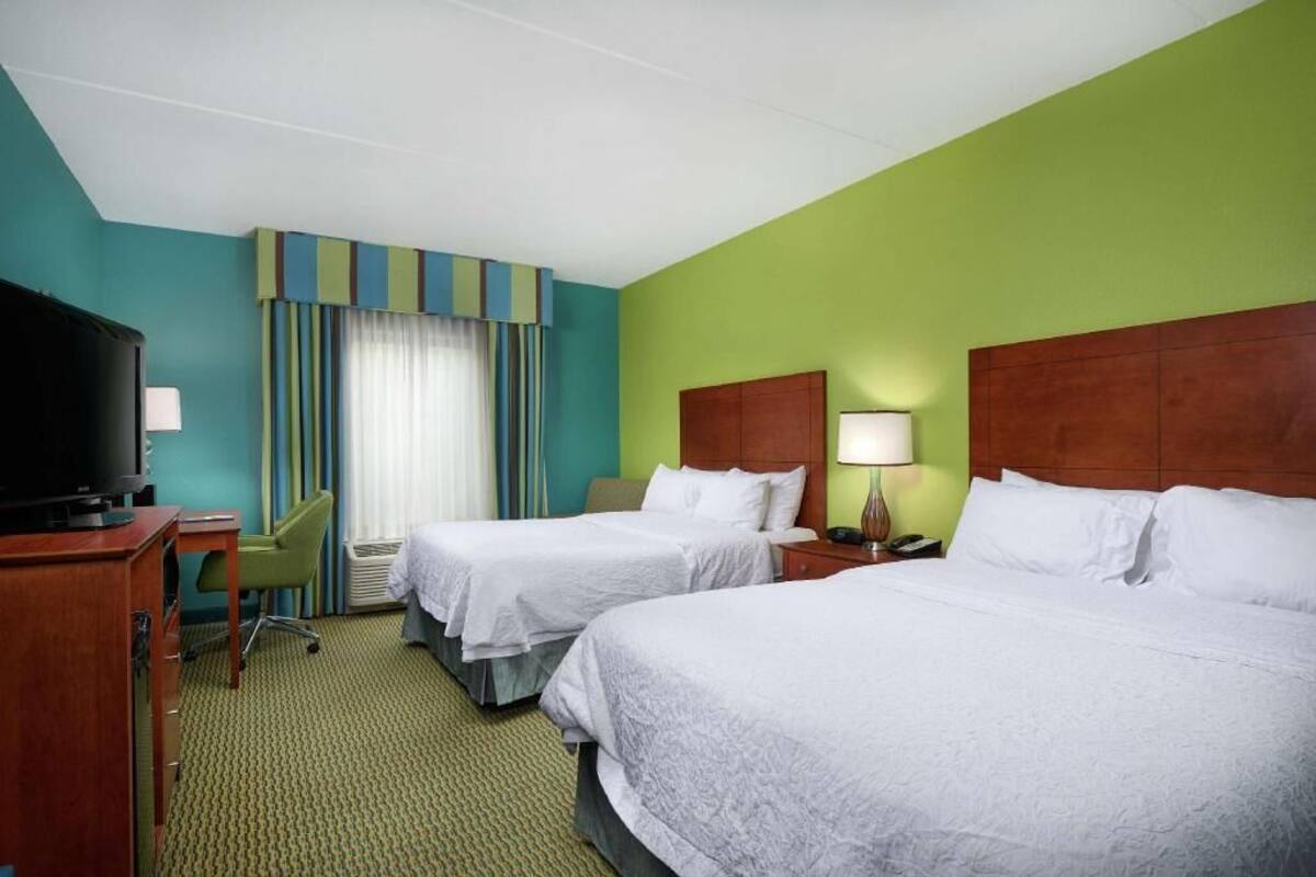 A hotel room with two beds, a TV, a desk, and a chair.