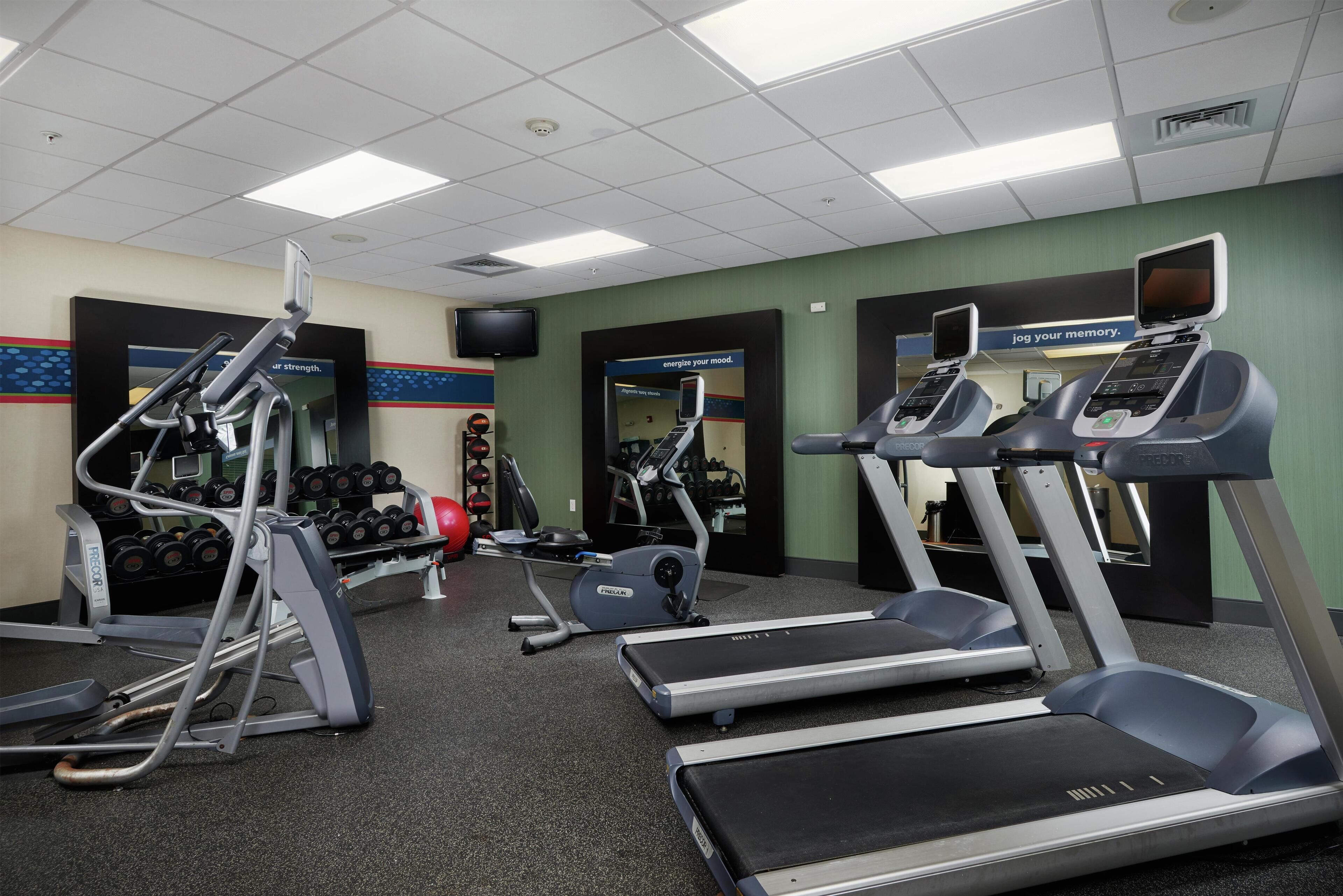 Une salle de sport équipée de tapis de course, d’appareils de musculation et d’haltères.