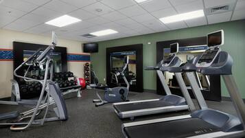 Une salle de sport équipée de tapis de course, d’appareils de musculation et d’haltères.
