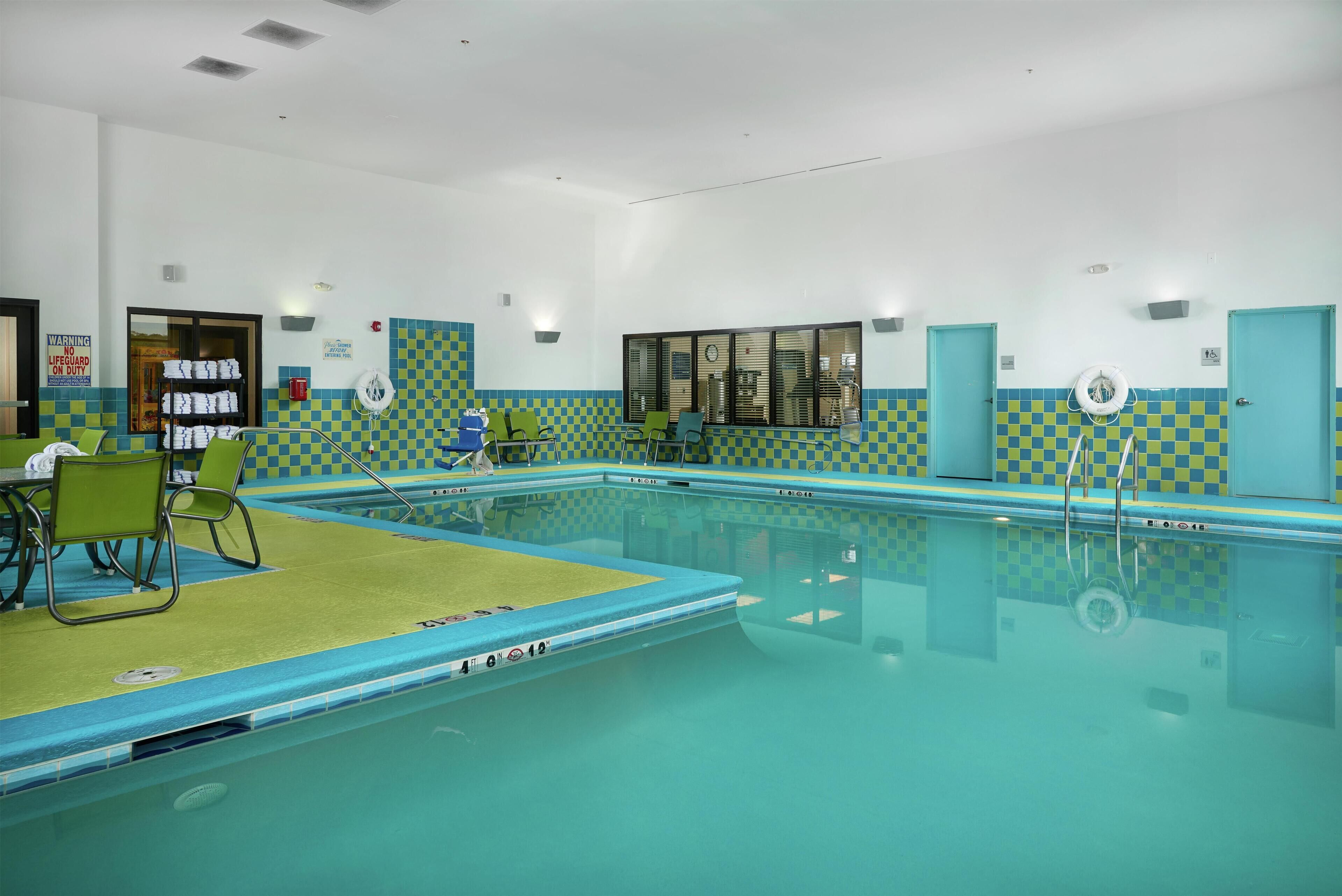 A swimming pool with checkered tiles, green chairs, and a lifeguard stand.