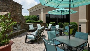 An outdoor patio with stone walls, green chairs, and tables under striped umbrellas.