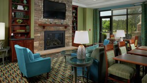 A hotel lobby with a stone fireplace, a television mounted above it, and seating areas with tables and chairs.