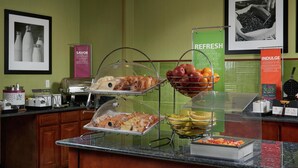 A breakfast buffet with various food items under glass covers, including fruits, pastries, and a tray of vegetables.