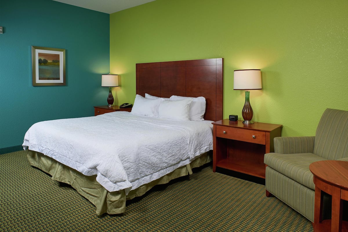 A hotel room with a large bed, two bedside tables with lamps, a chair, and a small table.