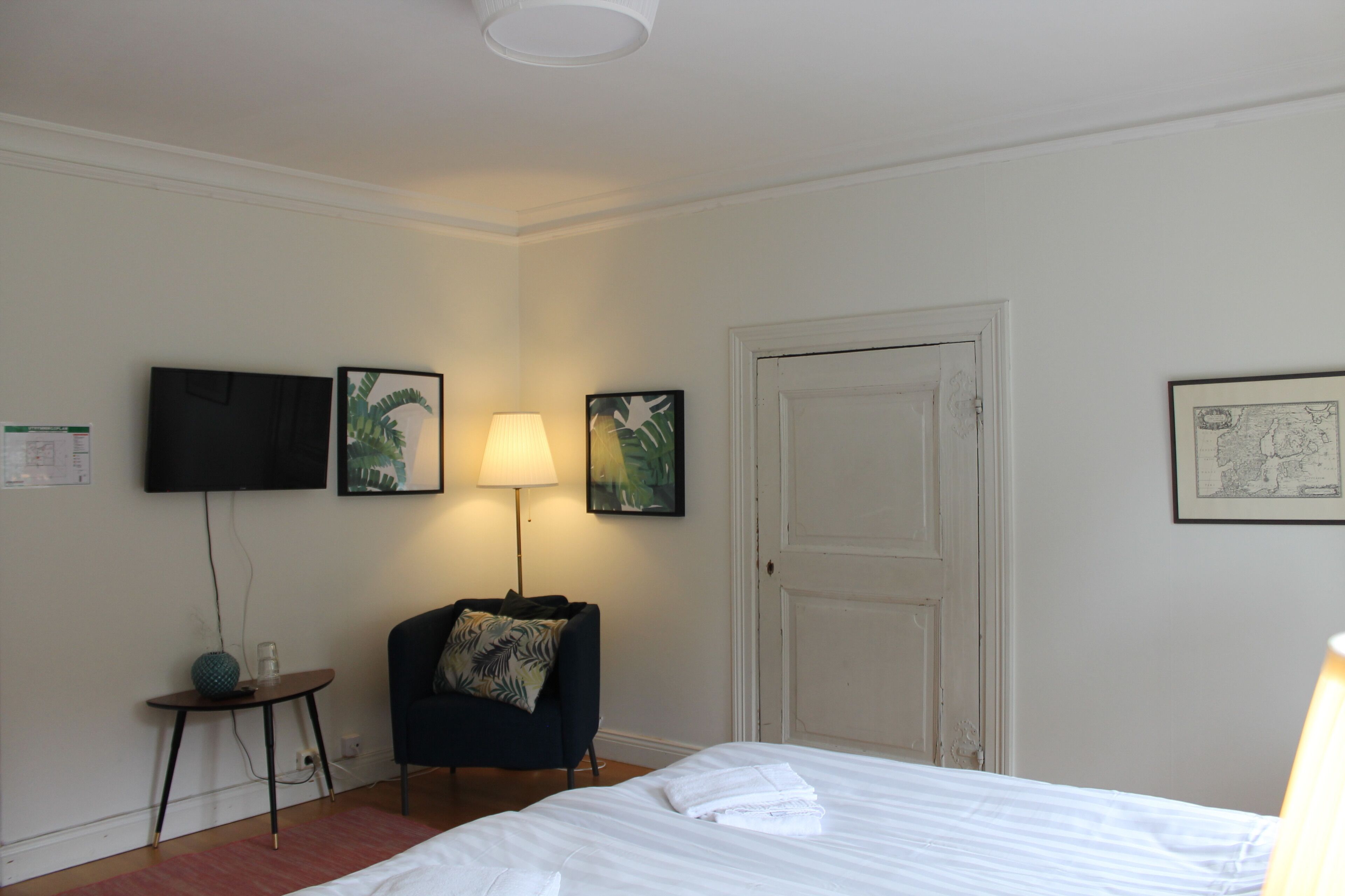 Habitación de hotel con cama, una silla, lámpara, televisión y obras de arte en las paredes.
