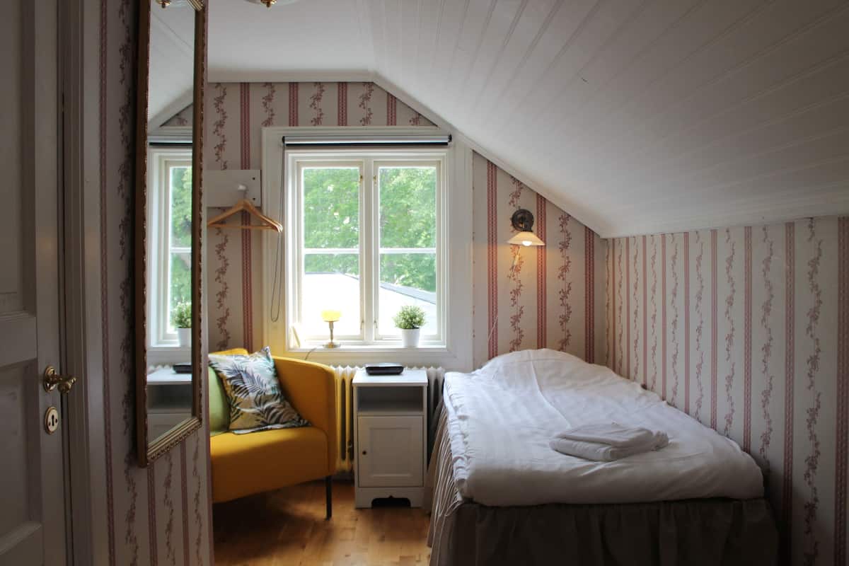 A bedroom with a bed, a desk, a chair, a window, and a door.