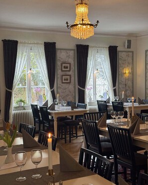 A dining area with tables set for four, each with wine glasses and candles, under a chandelier. - Wanbo Herrgard (Smedjebacken)