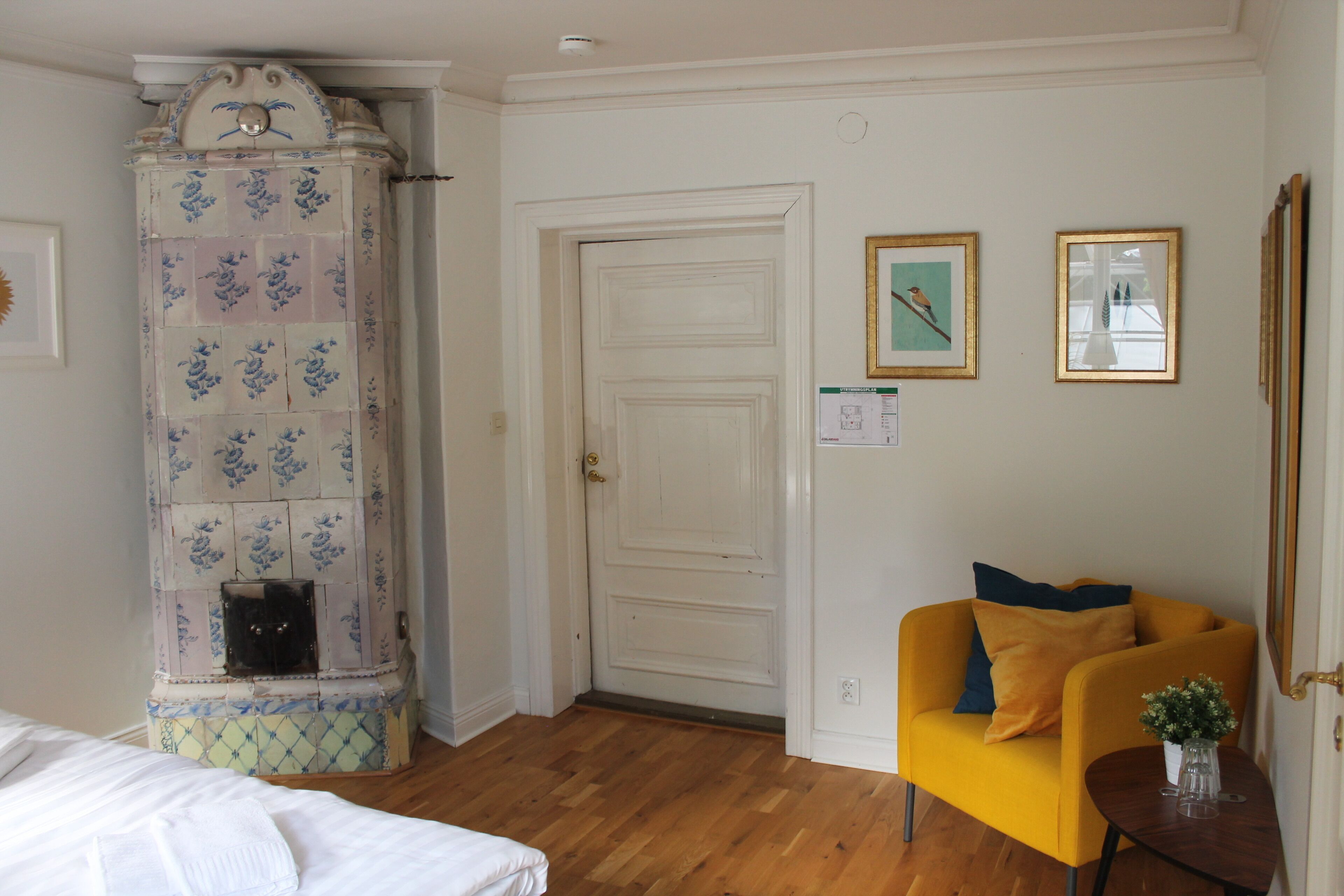 A room with a wooden floor, a white door, a yellow armchair, and a tiled fireplace.