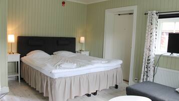 Quarto bem arrumado com cama, mesas de cabeceira, uma cadeira e janela com cortinas.