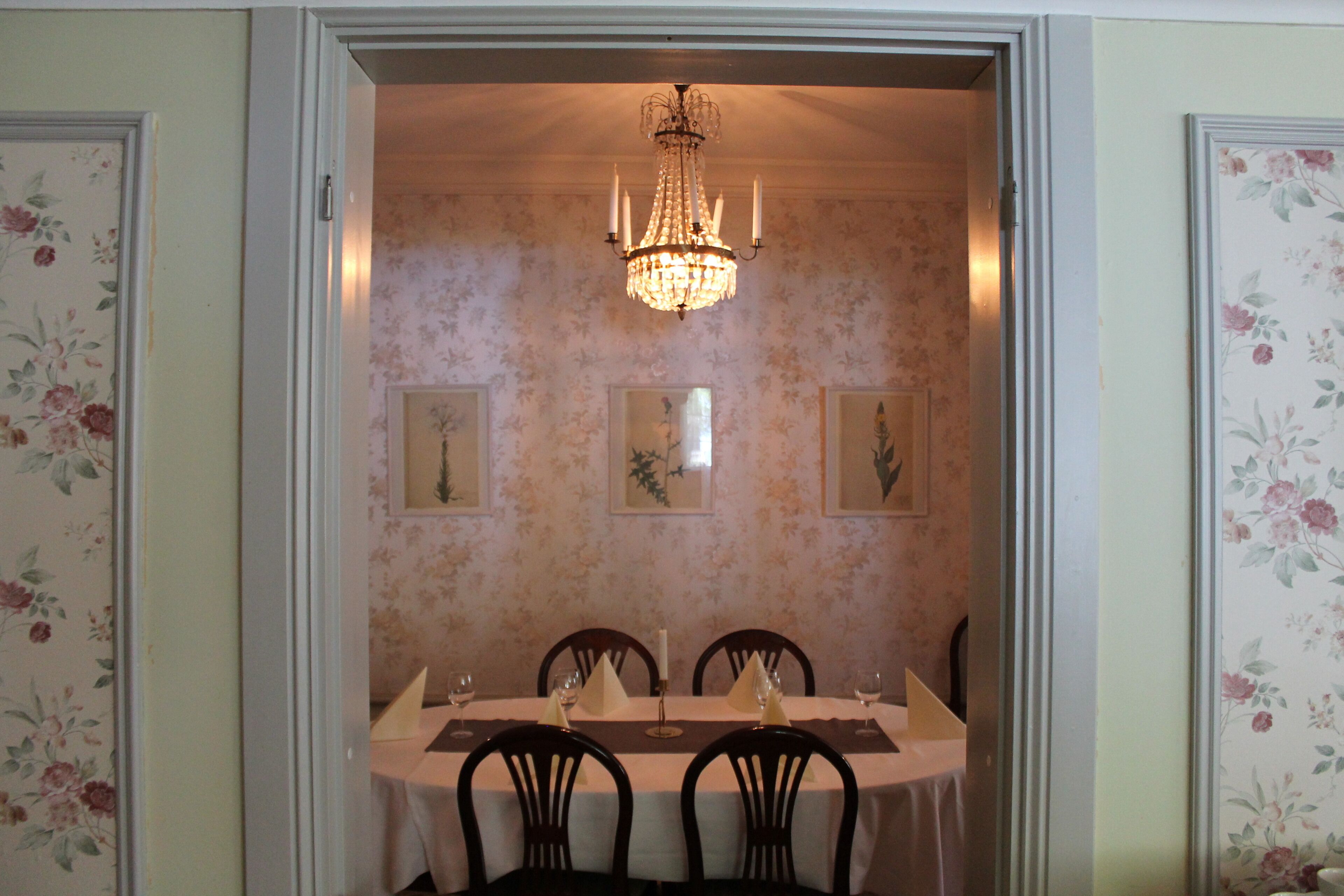 A dining room with a chandelier, floral wallpaper, and a table set for four.