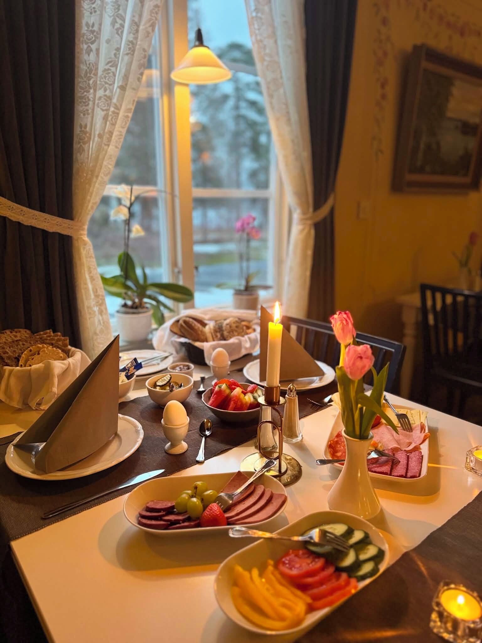 A breakfast setting with a variety of food items, a candle, and a vase with flowers.