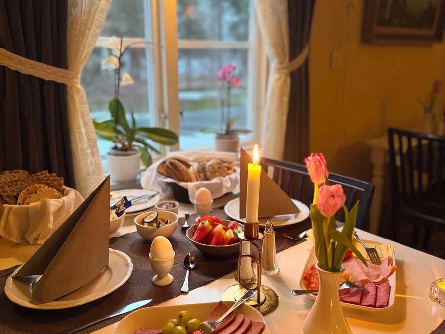 Ein gedeckter Frühstückstisch mit verschiedenen Speisen, einer Kerze und einer Blumenvase.