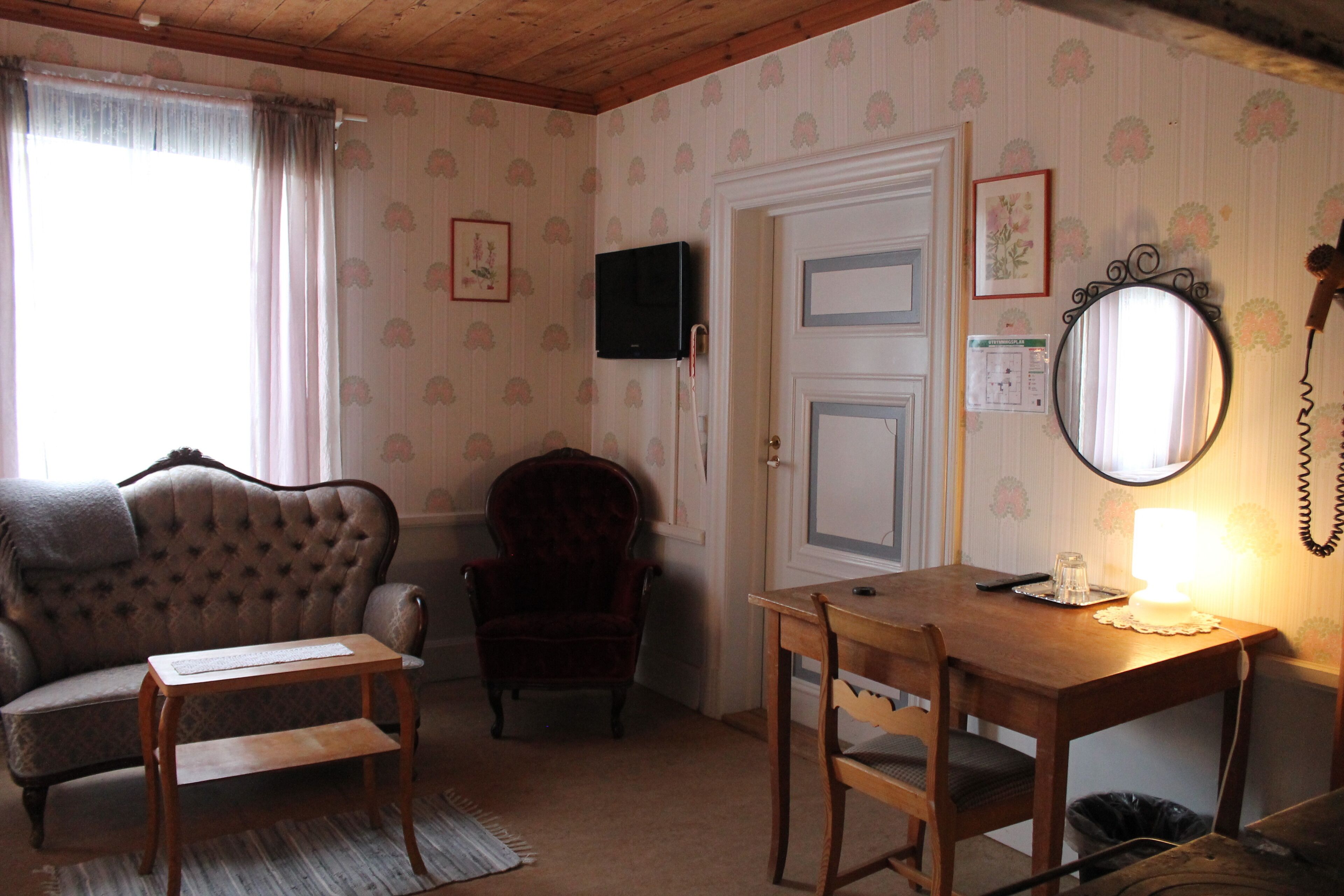 Una habitación acogedora con sofá, sillón, mesa de madera y televisor instalado en la pared.
