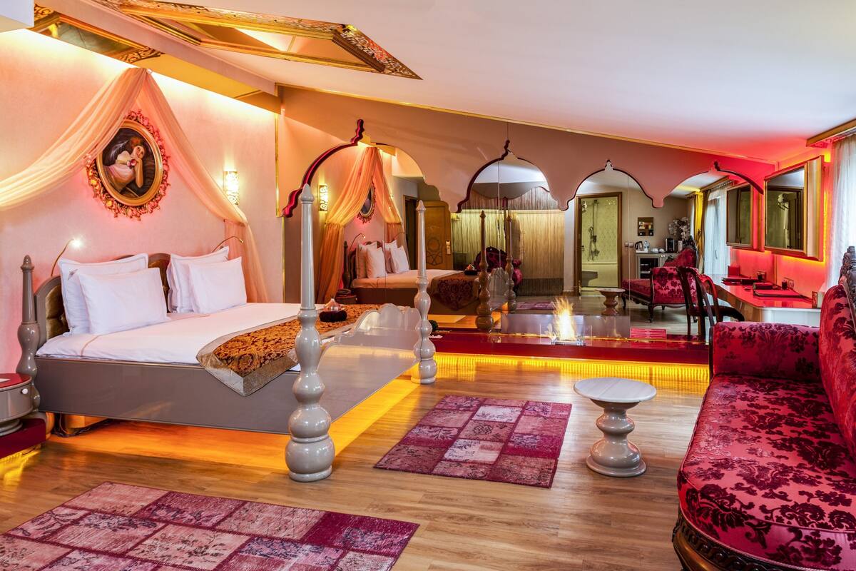 A luxurious bedroom with a canopy bed, a sitting area with a red sofa, and a dining area with a red table.
