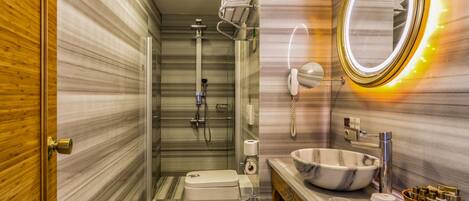 A modern bathroom with a marble floor, a white toilet, a glass-enclosed shower, a vanity with a marble sink, and a wall-mounted mirror with a light.